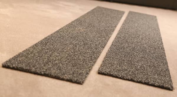 Deux échantillons de lames de moquette couleur grise posés sur le sol.