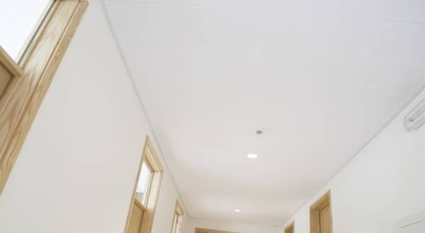 Vue en contre plongée d'un plafond métallique blanc dans les couloirs d'une entreprise avec portes en bois clair et murs blancs.