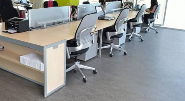 Vue d'ensemble d'un bureau d'entreprise avec sol en linoléum moucheté, grand bureau pour huit personnes, 8 fauteuils à roulettes.