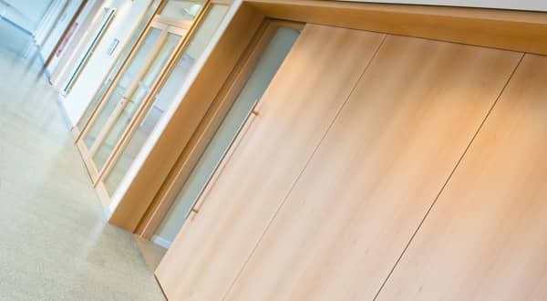 Cloison mobile en bois clair prise de biais, système de porte coulissante et accès double porte pour séparer trois espaces.