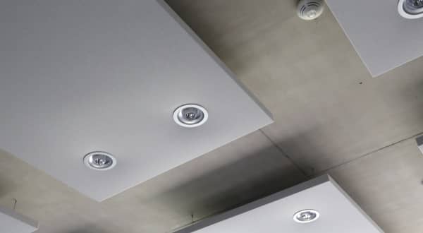 Zoom sur panneaux acoustiques gris avec spots de lumière intégrés sur plafond béton.