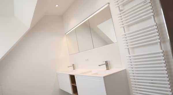 Cloison en plaques de plâtre enduites avec enduit fin dans une salle de bain blanche finalisée, double vasque, miroir, radiateur.