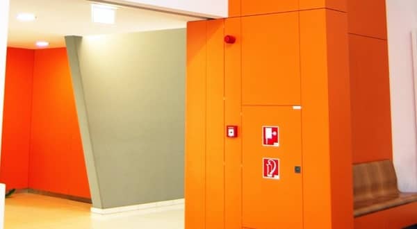 Vue d'ensemble d'un hall d'entrée avec cloison habillage stratifié couleur orange vif, caisson matériel incendie intégré, banc.