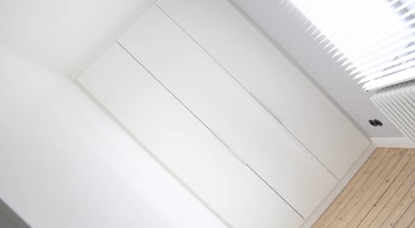 Dressing sur mesure blanc, trois grandes portes verticales fermées avec longues poignées métalliques fines, photo prise de biais.