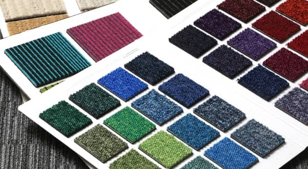 Échantillons de moquette divers coloris dans un classeur ouvert sur le sol recouvert de moquette grise.