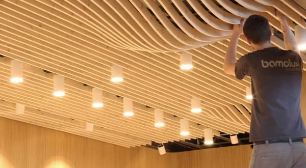 Poseur Bamolux qui installe un plafond suspendu en lames de bois clair avec formes de bulle à certain endroit et spots intégrés.