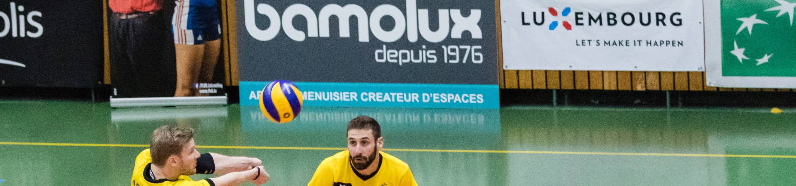 Photo pour illustrer les sponsoring. Deux joueurs du Volley Club Strassen envoilent la balle avec panneau sponsor Bamolux en fond.